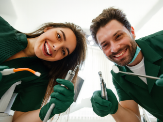 Zwei Zahnärzte beugen sich lächelnd über die Kamera