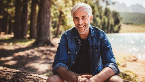 Älterer Mann sitzt lächelnd am Ufer